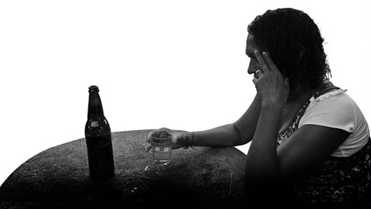 Mulher sentada diante de uma garrafa de cerveja